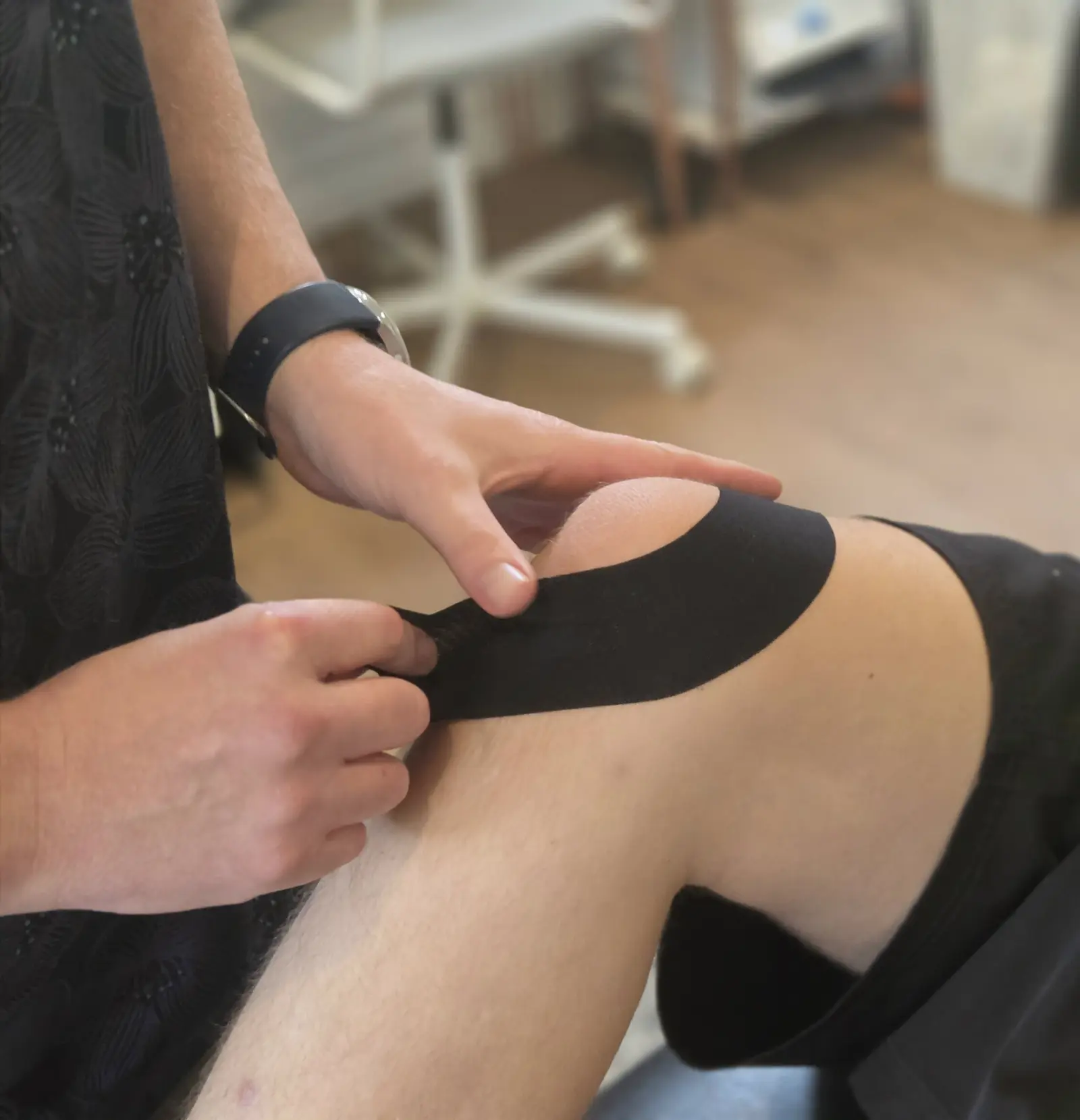 Hands applying black kinesiology tape around a knee