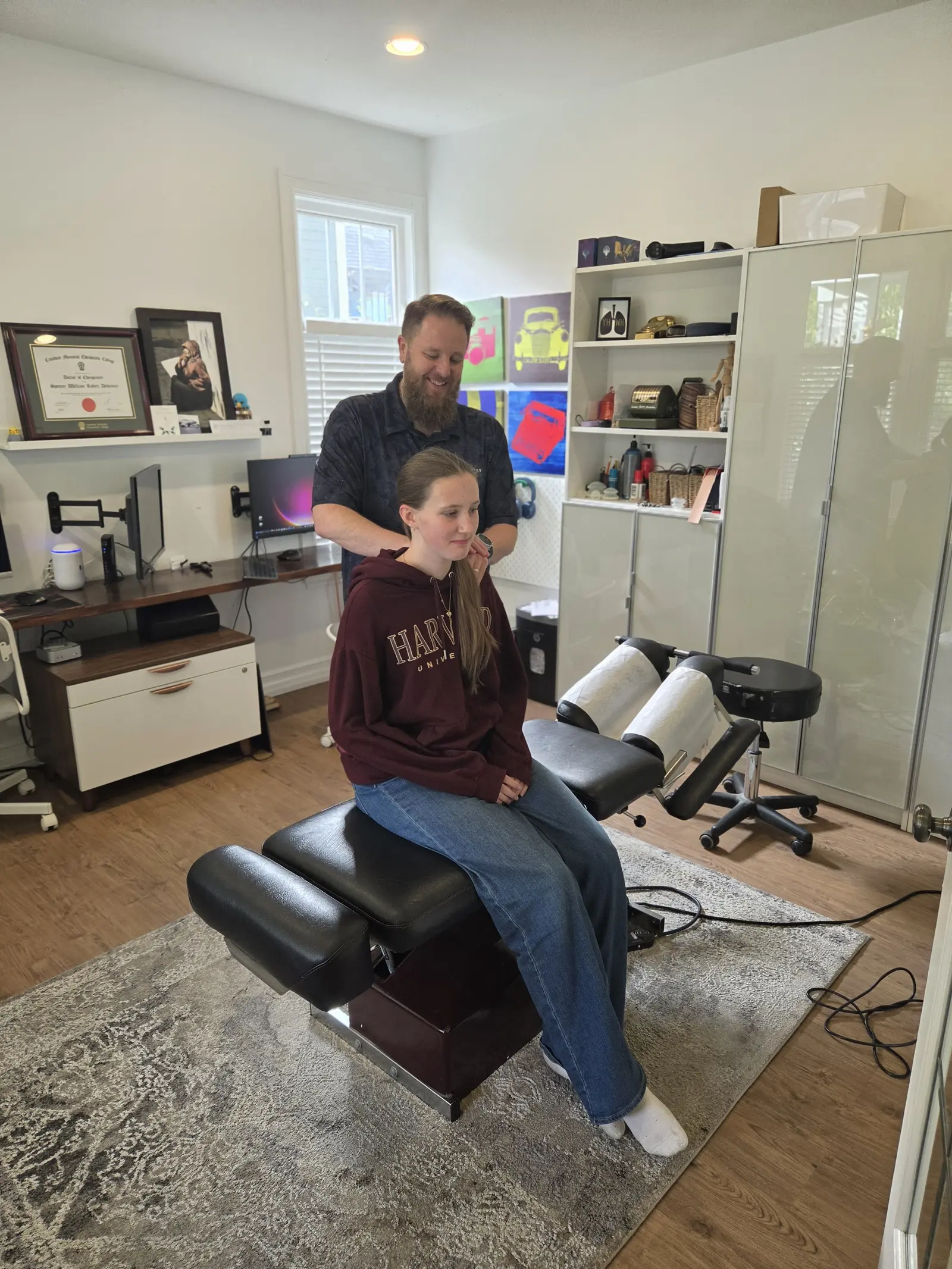 Dr. Devenney standing behind a patient seated on the treatment table, his hands on her neck